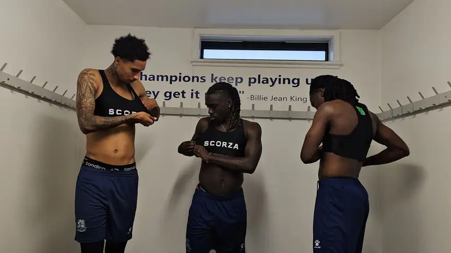 Three teammates pulling on Scorza performance vests in the changing room