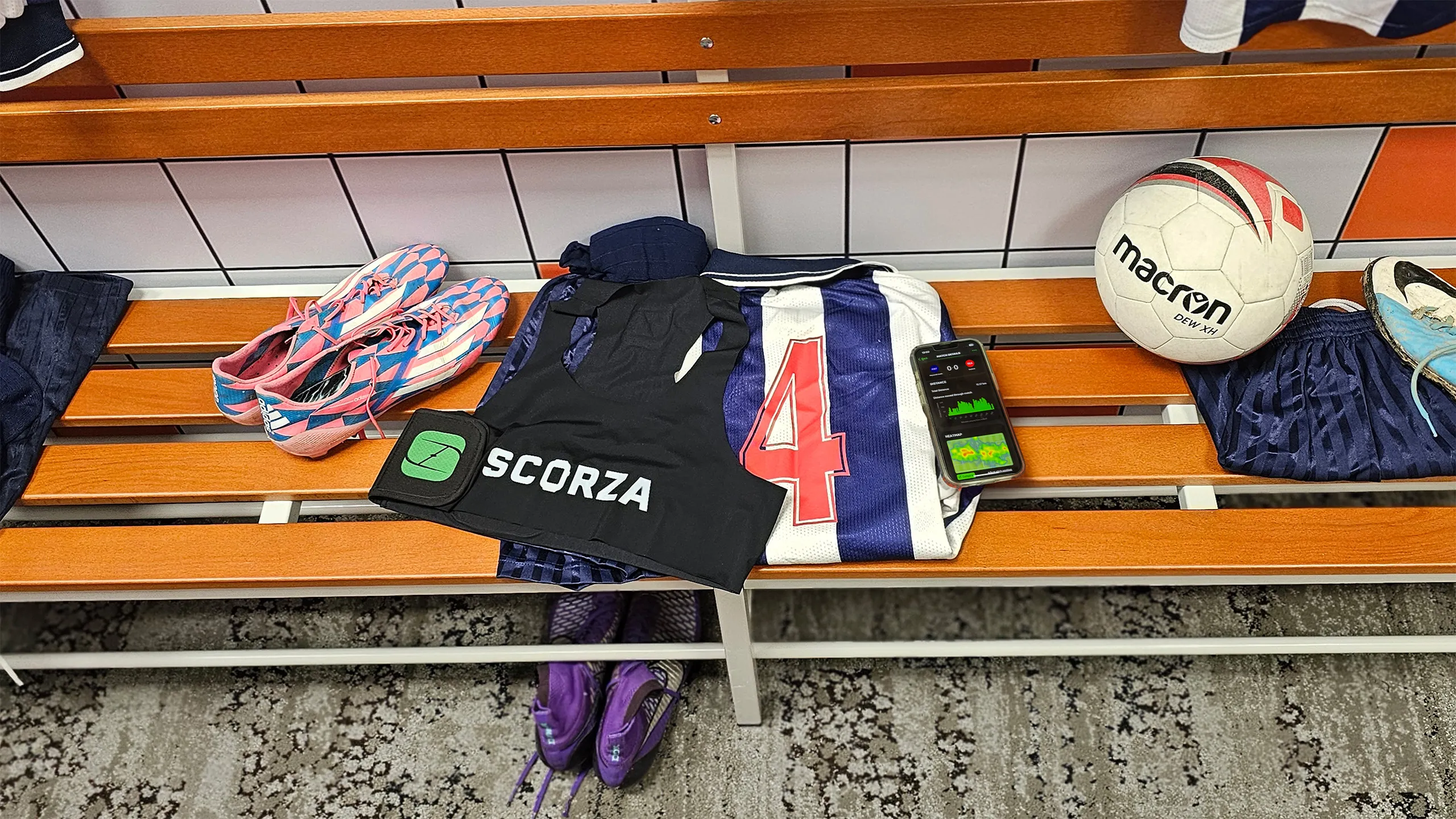 A player's kit on the changing-room bench beside a phone showing their heatmap and distance